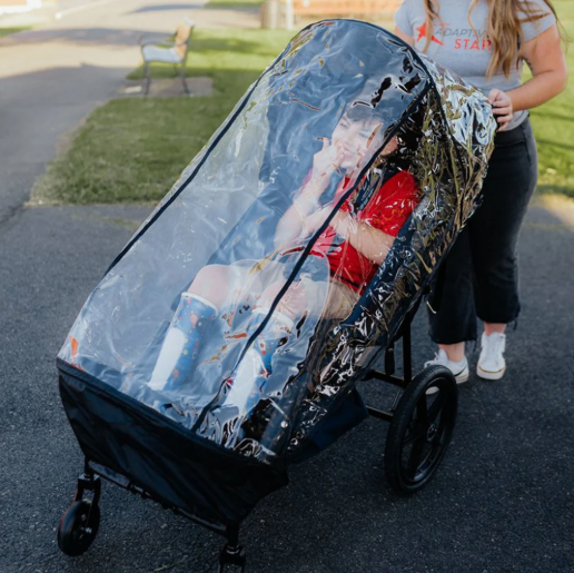 Caregiver pushing a child in an Adaptive Star chair with rain canopy outdoors