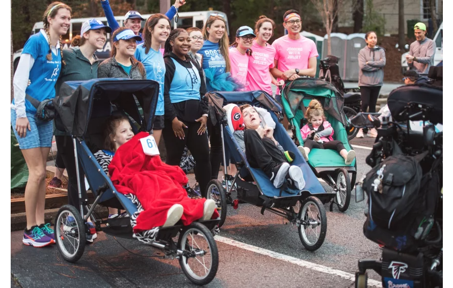 Children and caregivers with adaptive push chairs at an inclusive road race